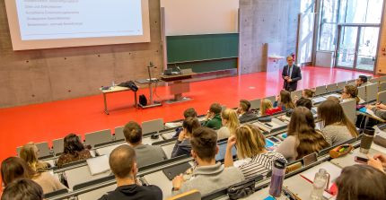 A man stands in a lecture hall in front of many students and gives a lecture
