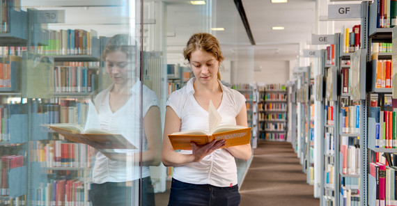 Studentin steht in der UB und blättert in einem Buch