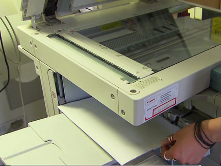 Hand zieht ein Blatt Papier aus dem Drucker